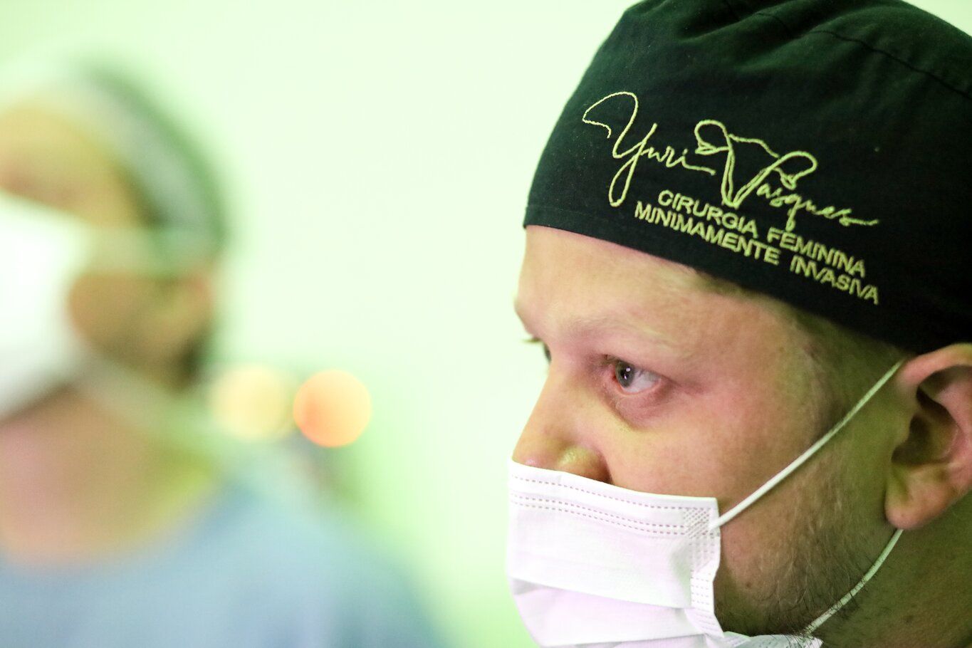 Dr. Yuri Vasques de perfil, de máscara e touca bordada com seu nome